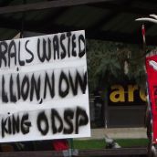 A sign at the Friday afternoon rally opposing potential attacks on disability benefits by the provincial Liberal government, next to the staff of the Indigenous Student Circle of Laurentian University. (Photo by Scott Neigh)